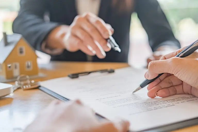 A person is writing on paper with another person holding a pen.