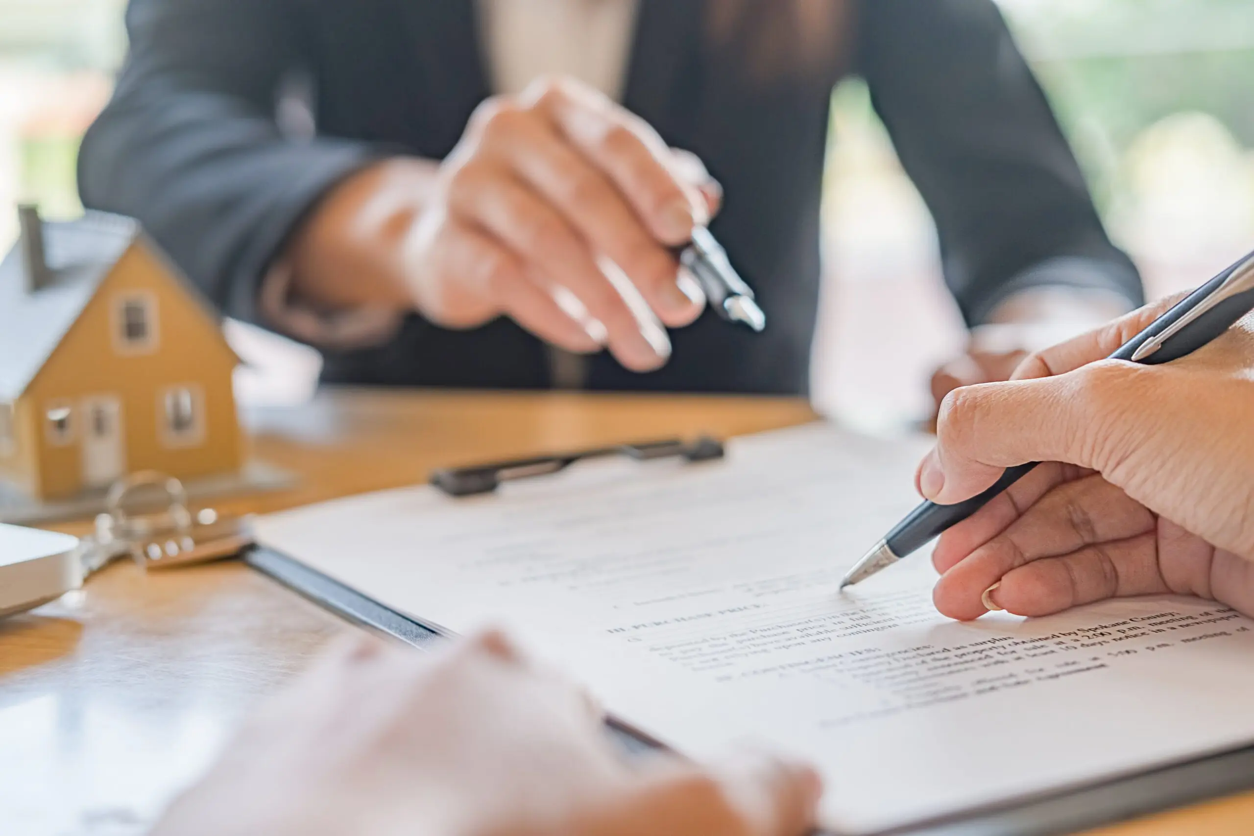 A person is writing on paper with another person holding a pen.